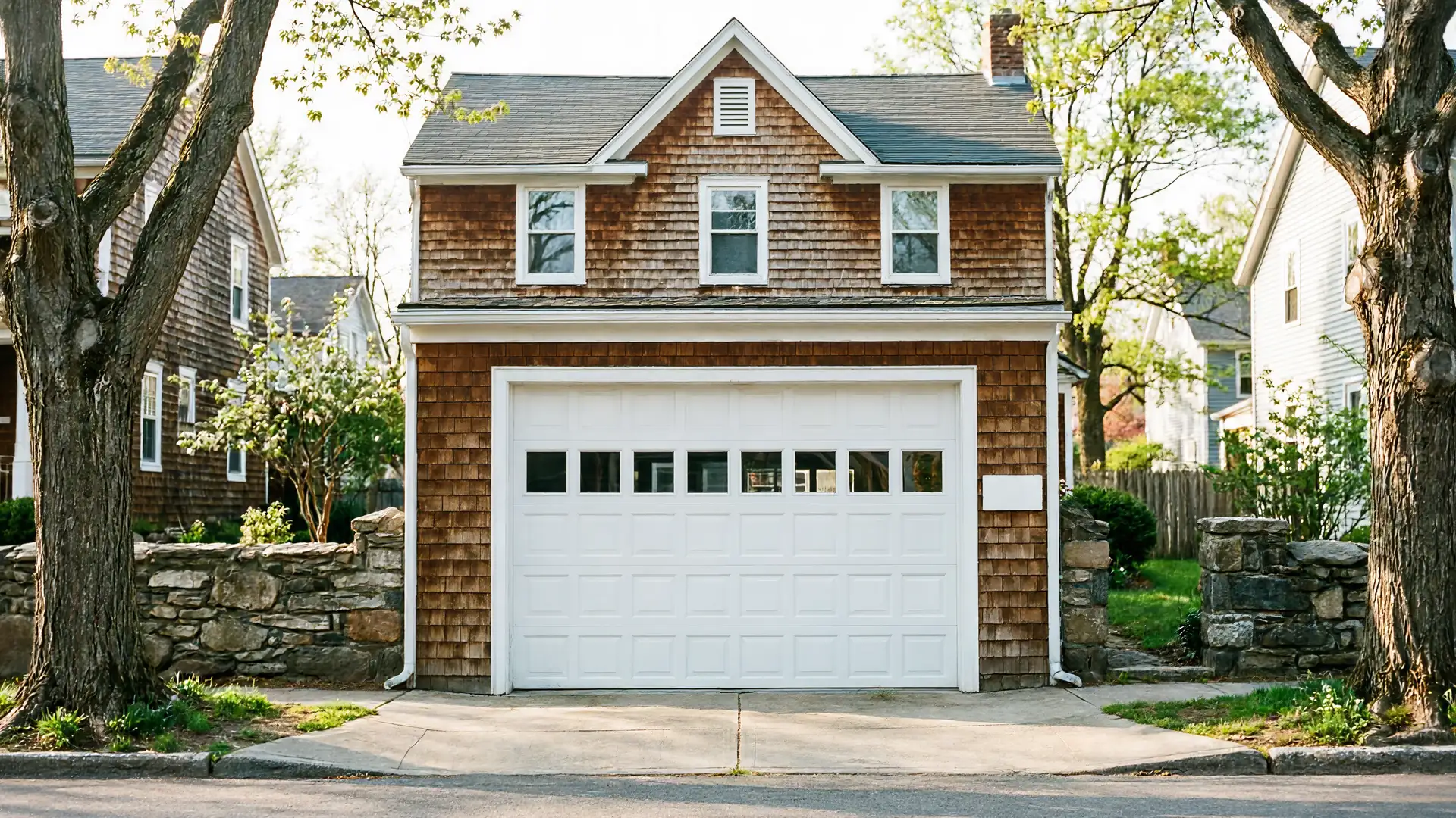 A white garage door with windows is on a brown shingled house.